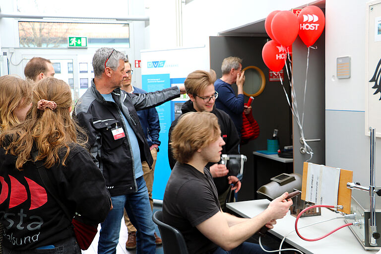 Junge Menschen beim Campustag 2023 um einen Versuchsaufbau versammelt, teils im Gespräch 