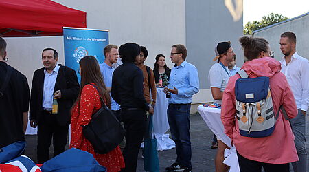 eine Gruppe von Menschen steht zusammen auf dem Campus der Hochschule - in Grüppchen im Gespräch und vor einem roten Pavillon