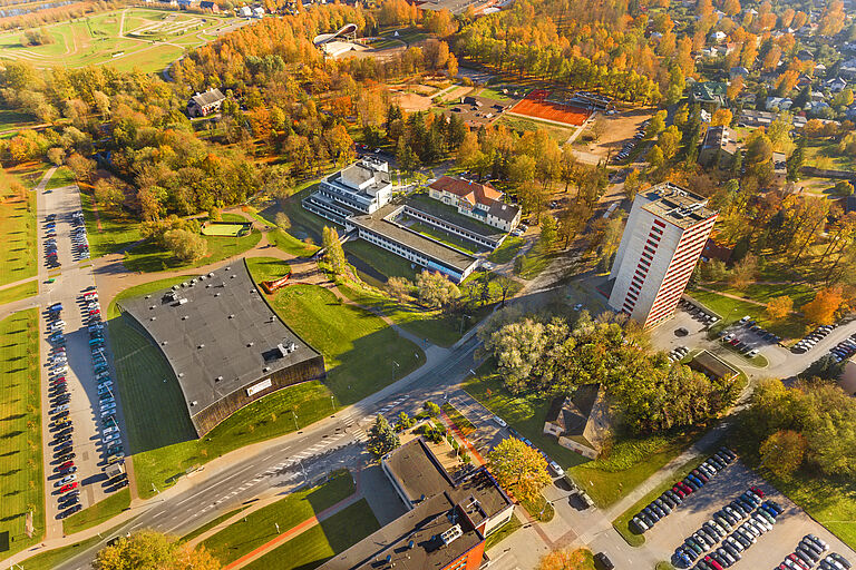 Luftaufnahme von einem bewaldeten grünen Hochschulcampus, mit mehreren Gebäuden und Parkplatz