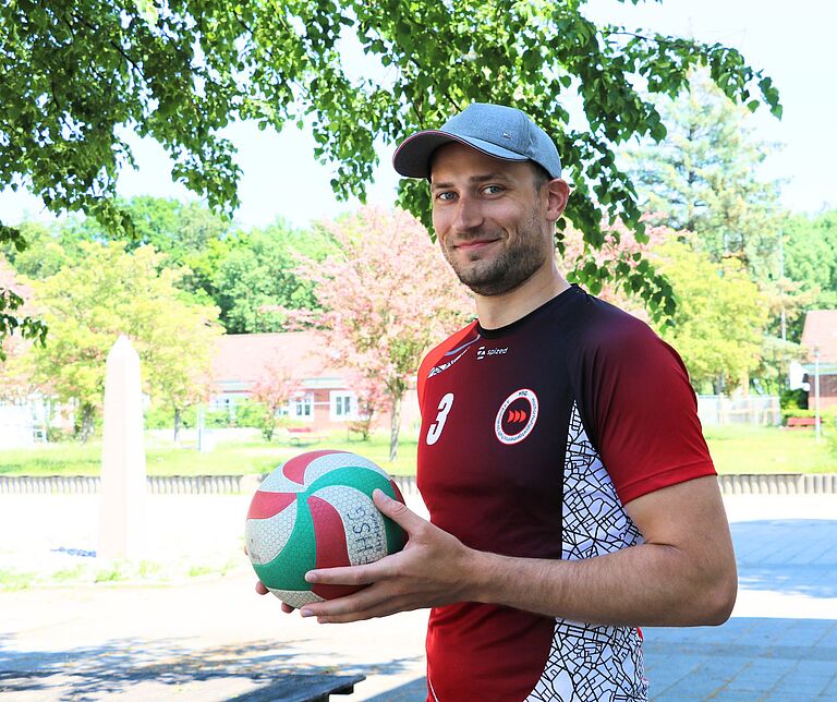 ein junger Mann mit einem Volleyball schaut freundlich in die Kamera