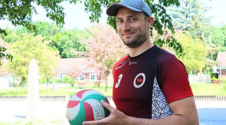 ein junger Mann mit einem Volleyball schaut freundlich in die Kamera