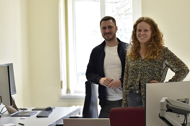 Anna Elisa Völz und Johannes Mai von NOX AAL Technologies stehen in einem Büro, sie vorn, er knapp dahinter, beide lächeln in die Kamera.