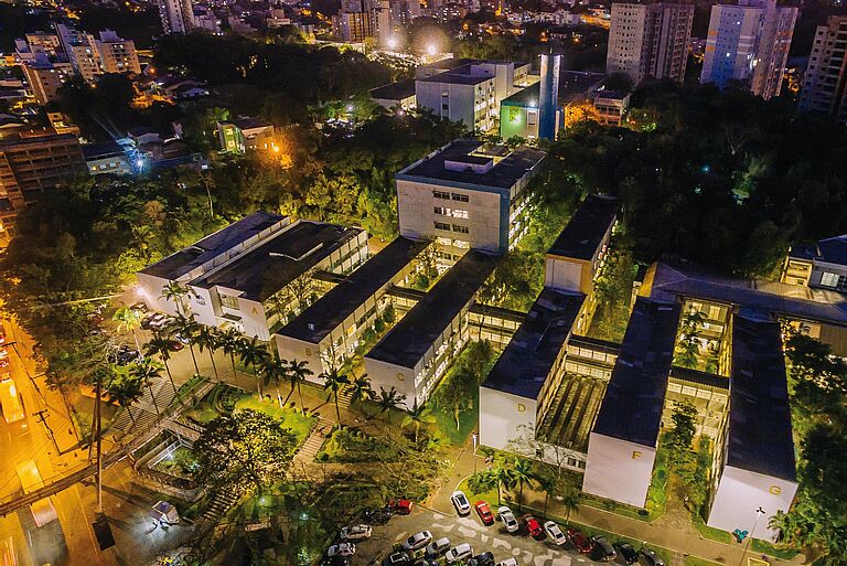 eine Aufnahme von oben zeigt mehrere Gebäude, die Universität Blumenau, bei Nacht, mit hellen Lichtern und dem Blick auf Palmen