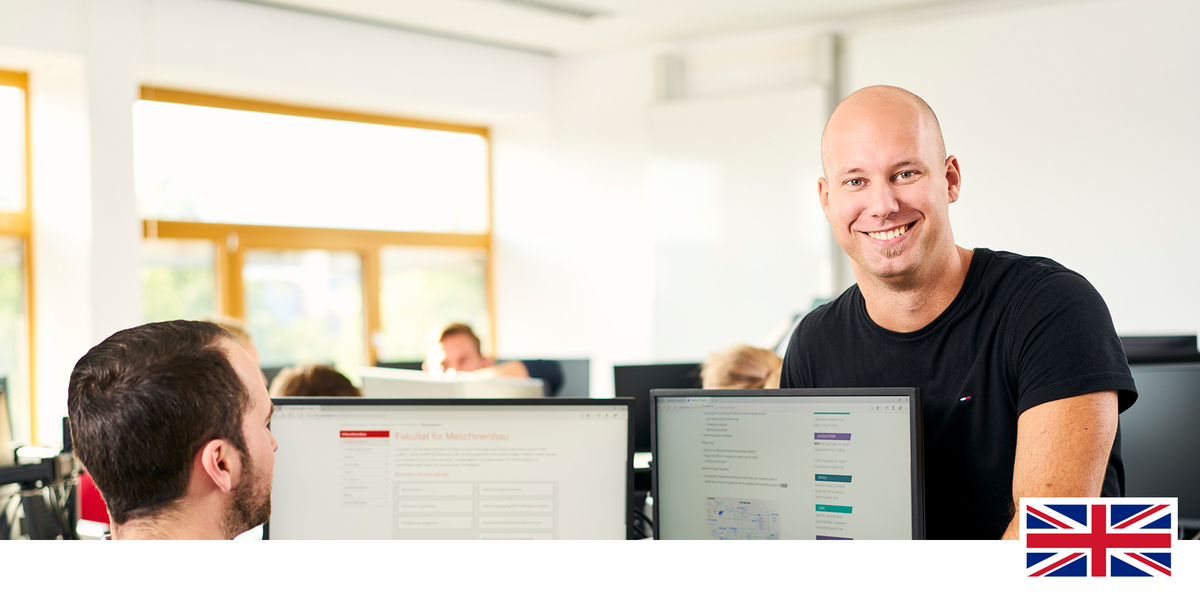 Headerfoto: Student sitzt im PC-Pool und lächelt in die Kamera