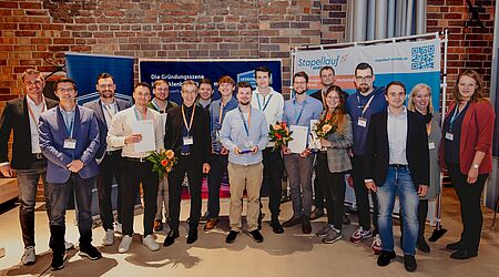 Ein Gruppenfoto zeigt Sieger*innen, Sponsor*innen und Juror*innen aus dem Businessplanwettbewerb „SEGEL SETZEN!“ gemeinsam stehend mit Blumen. 