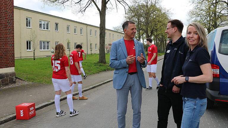 Drei Personen im Gespräch (Intero-Vertreter und der Rektor), im Hintergrund Fußballspieler