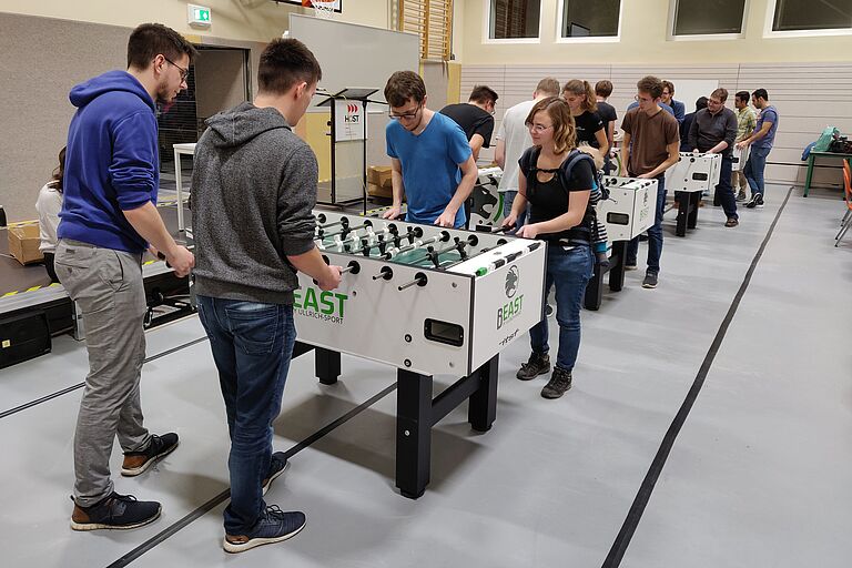 Viele junge Menschen stehen in Teams an Tischfussballtischen