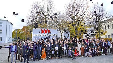 Ein Gruppenbild von jungen Menschen, die schwarze Absolventenkappen in die Luft werfen