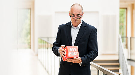 Prof. Dr. sc. hum. Dipl.-Ing. Holger Specht steht in der Mitte mit Würfel in der Hand