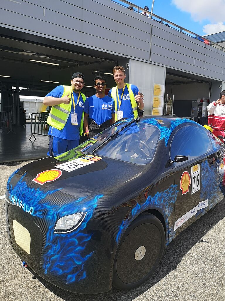 drei team-Mitglieder vor dem Bengalo, einem runderen Rennwagen, stehend