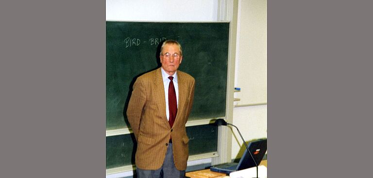 Bild von einem Mann vor einer grünen Tafel in einem Hörsaal, eine ältere Fotografie,
