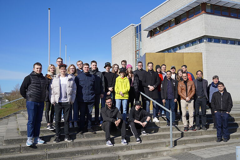 Eine Gruppe von vornehmlich jungen Menschen steht vor großen einem goldenen Würfel auf einem Gruppenbild - die Studierenden und einige Dozierenden der Spring School. 