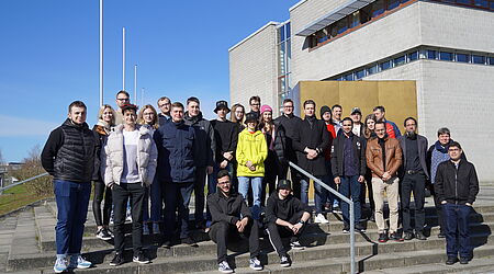 Eine Gruppe von vornehmlich jungen Menschen steht vor großen einem goldenen Würfel auf einem Gruppenbild - die Studierenden und einige Dozierenden der Spring School. 