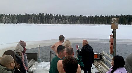 Menschen am Rande eines zugefrorenen Gewässers vor einer Waldkulisse - der Auftakt zum Eisbaden.er