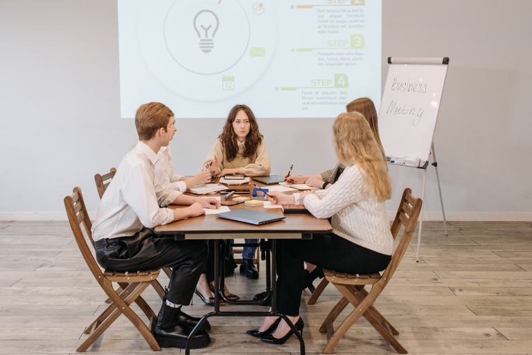 Einige junge Menschen sitzen an einem vermeintlichen Besprechungstisch vor einer Beamerprojektion.