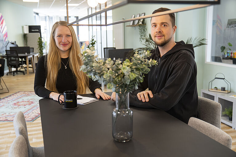 Eine Frau, Doreen Mdlodzik, und ein Mann, Lennart Deorocki, sitzen an einem Tisch.